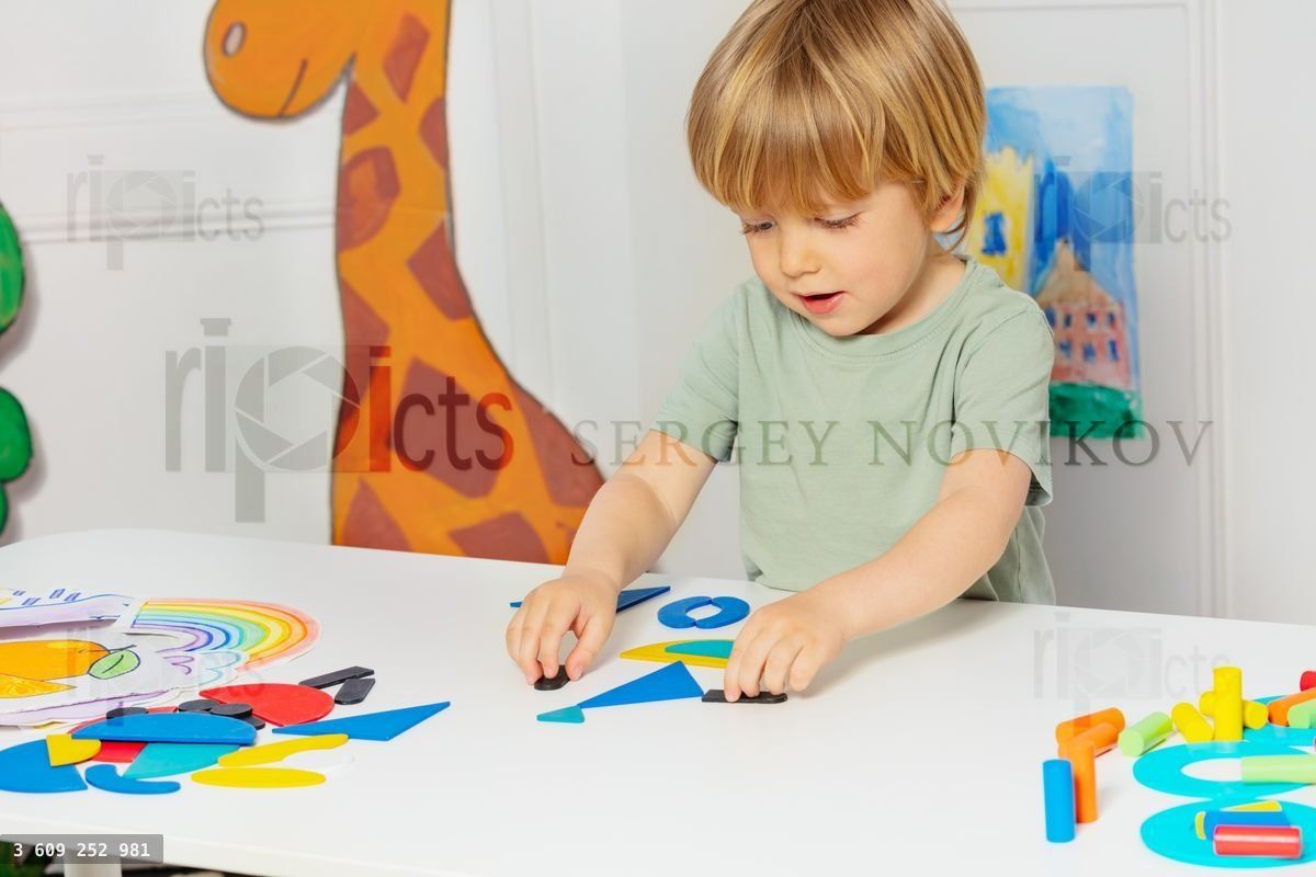 Blond boy form shapes standing by the table in kindergarten