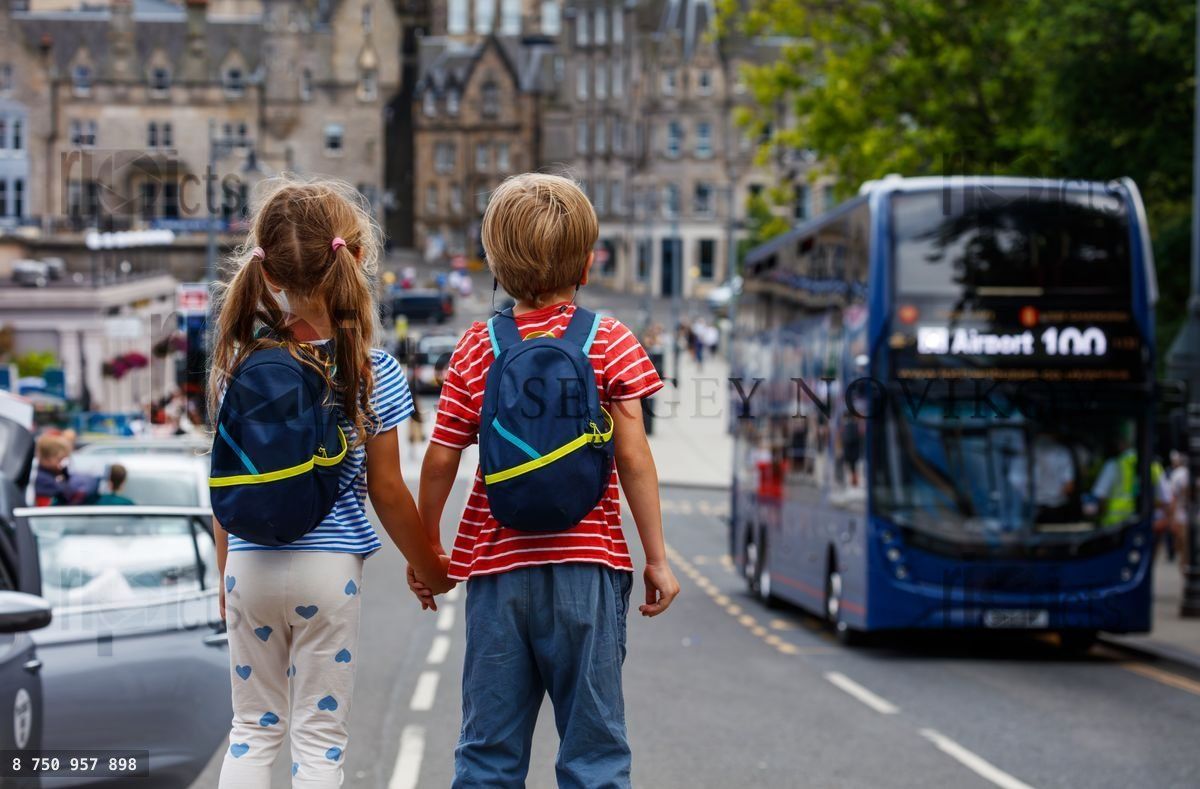 Des enfants se tenant par la main, regardant un bus dans une rue urbaine animée