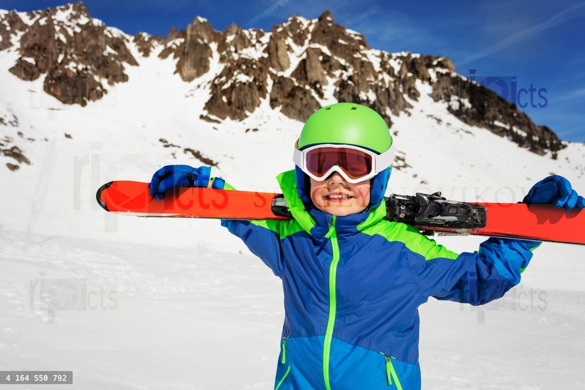 Happy boy with ski on shoulders over mountain rock