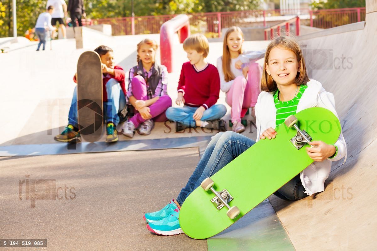 Kids sit behind and girl in front with skateboard