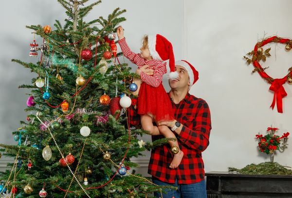 Child and dad decorate Christmas tree together hang ornaments