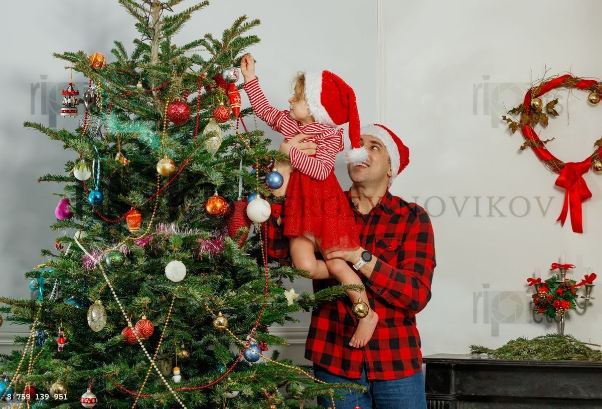 Child and dad decorate Christmas tree together hang ornaments