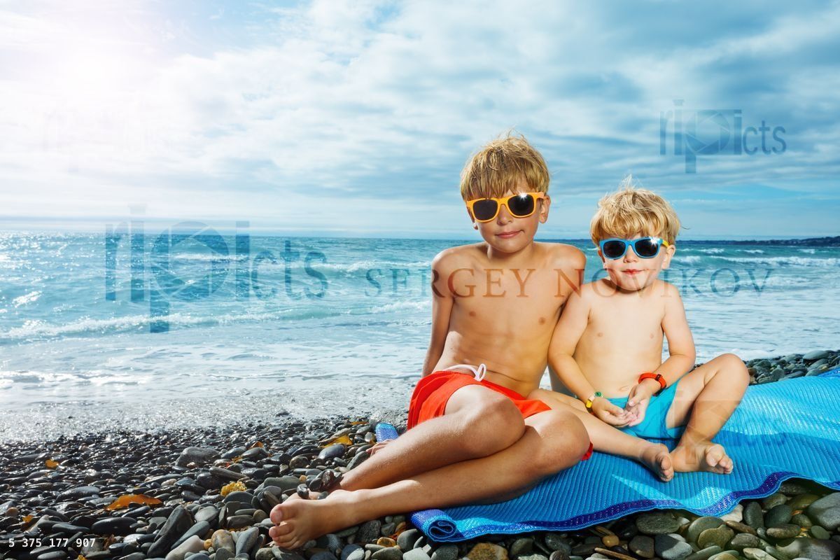 Boys, brothers sit together wrapped on pebble beach over the sea