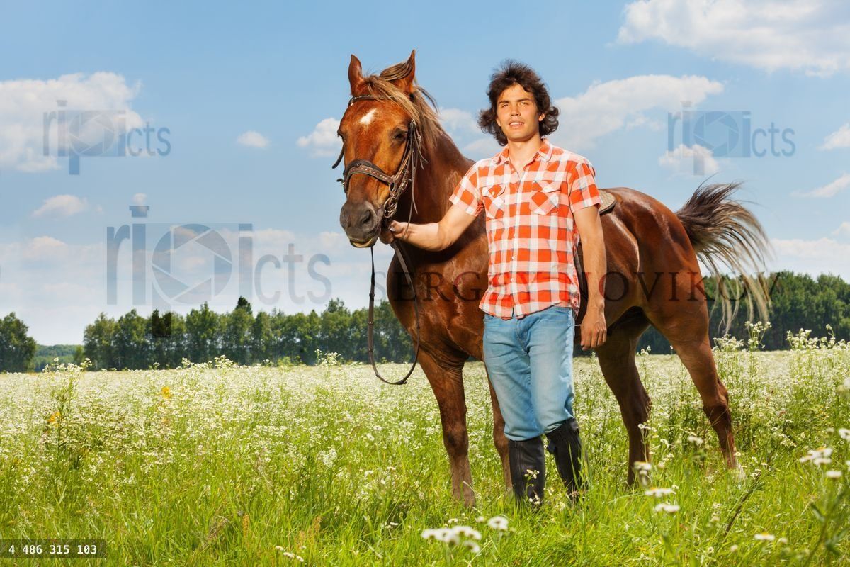 Young man holding his brown horse by a bridle