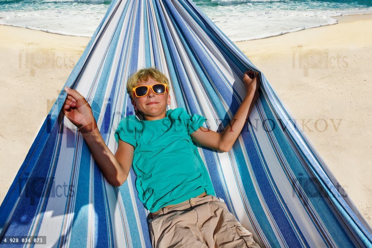 Boy with sunglasses lay in hammock on the sand beach