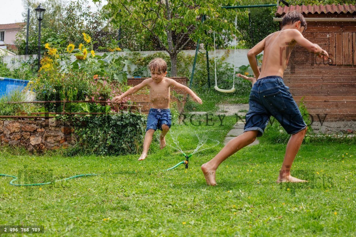 Young boys enjoy refreshing splash run around garden sprinkler