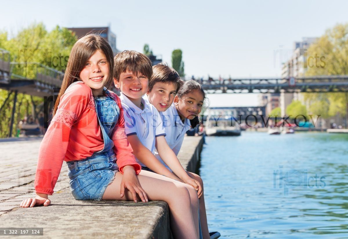 Four happy friends sitting in a line on embankment