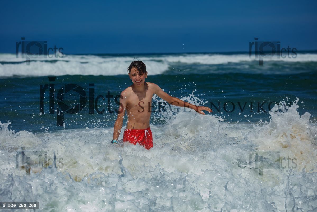Young boy teen laughing, playing in ocean waves at the beach