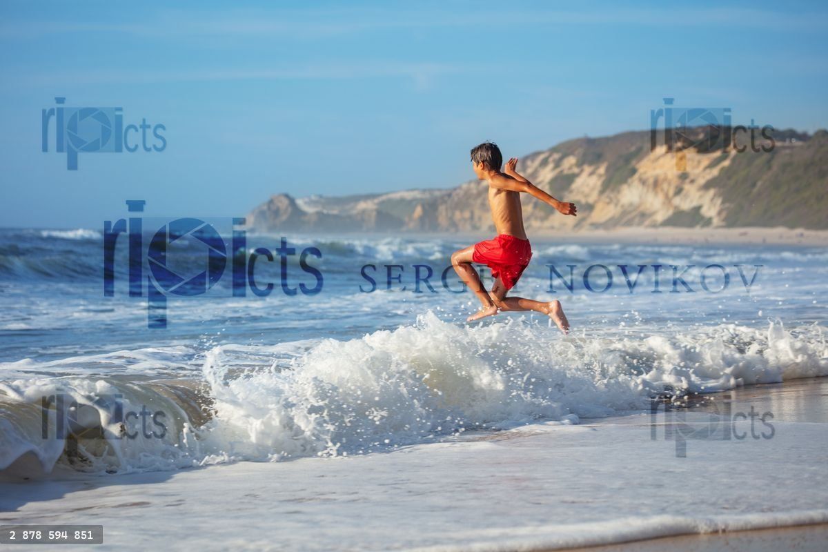 Youngster enjoys a beach run and jump among foamy strong waves