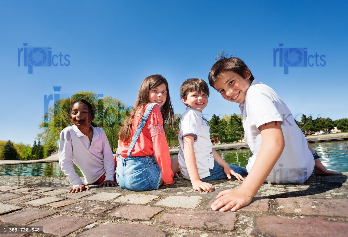 Four kids sitting on embankment during summer time
