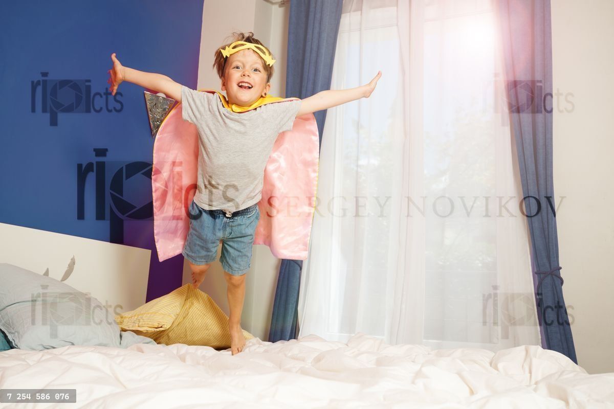 Un garçon en costume de super-héros sautant sur le lit des parents, plein de joie