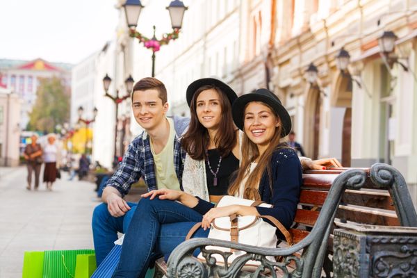 Three friends sit together on bench outside