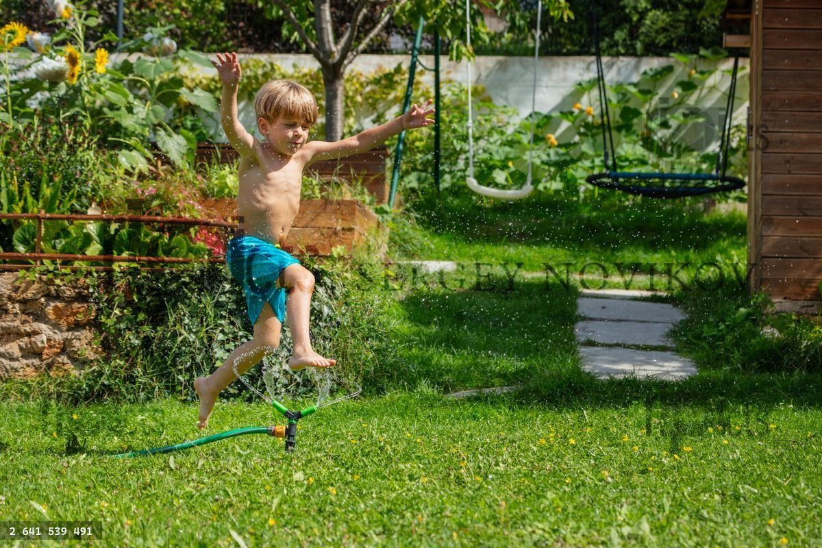 Young boy joyfully jumping over a sprinkler in the green garden