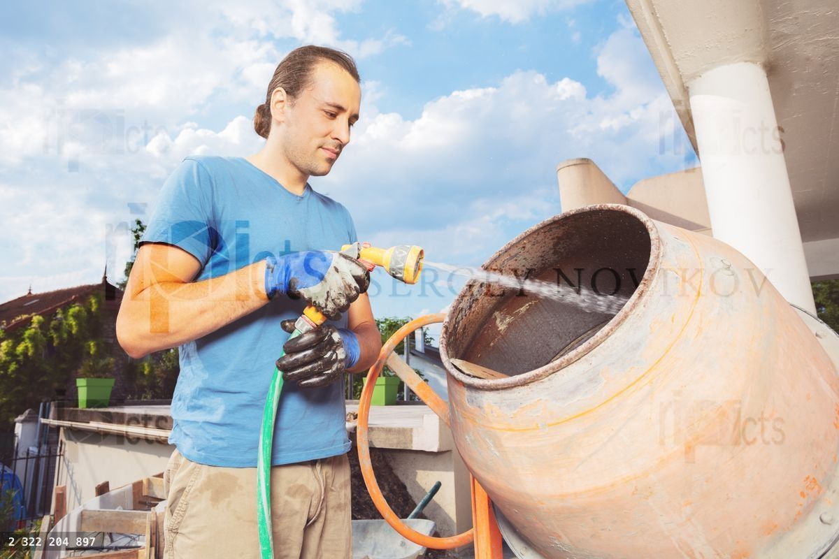 Young man stand cleaning cement mixer at home construction works