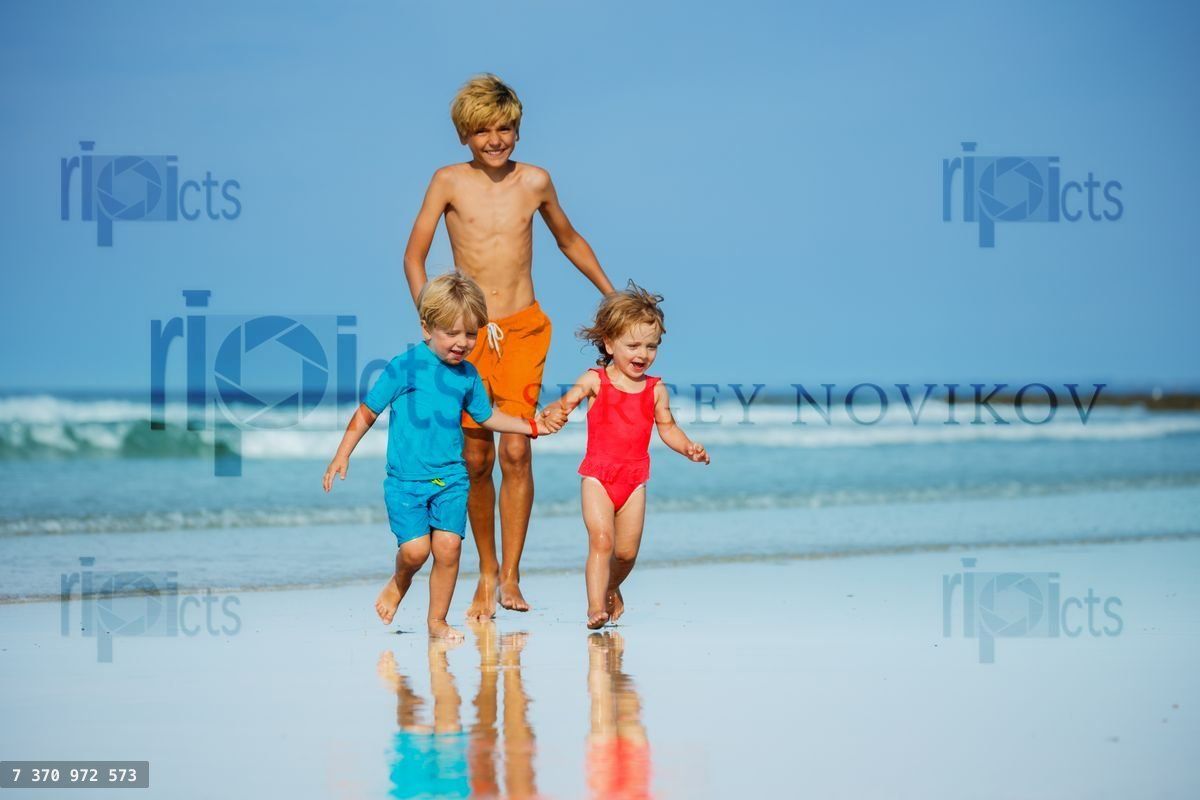 Group of three children run on sand beach holding hands