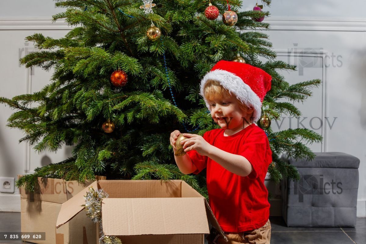 Excited little boy decorating a Christmas tree wearing Santa hat