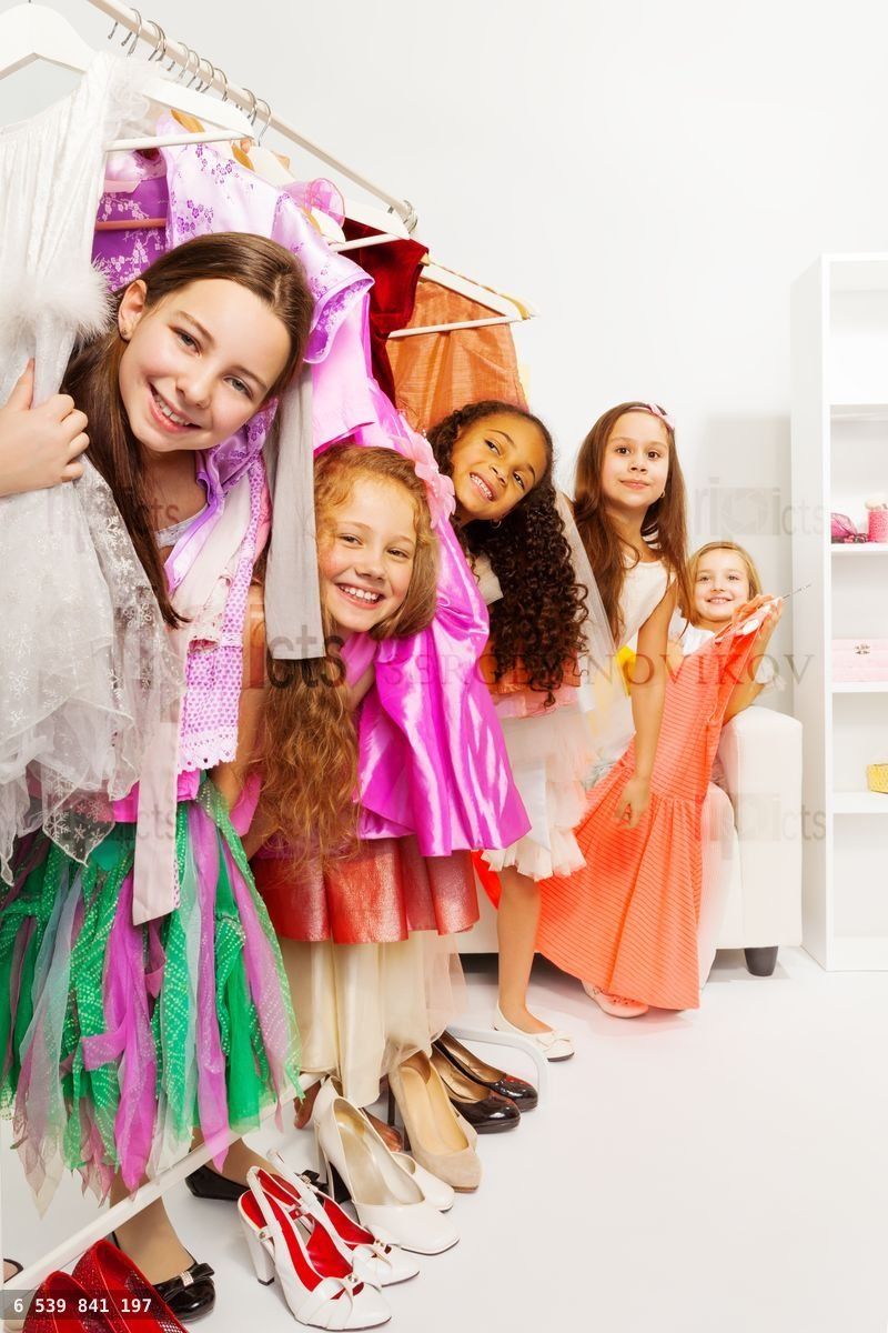 Happy small girls in store standing among dresses