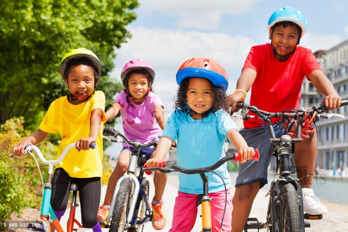 Happy African siblings riding bikes in summer city
