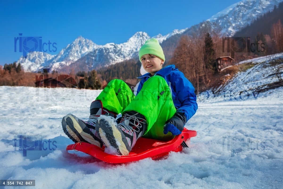 Young boy in winter outfit slide downhill on alpine slope