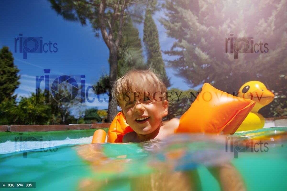 Funny kid in water with float armbands have fun at summer pool