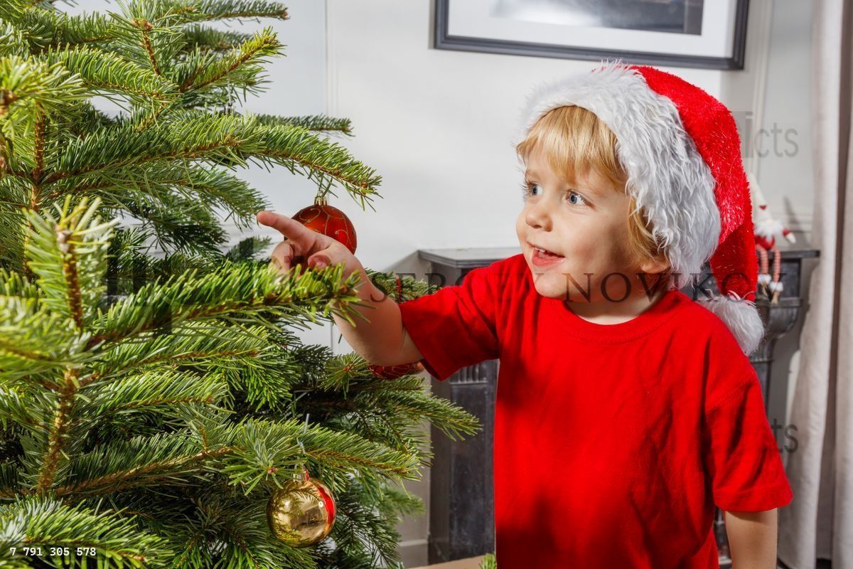 Enfant avec un bonnet de Père Noël et une chemise rouge pointe avec enthousiasme vers une décoration