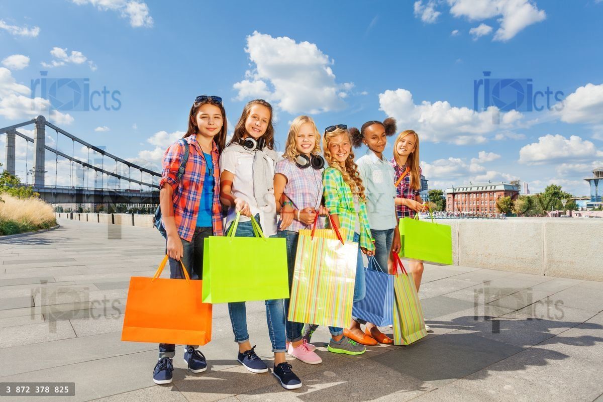 Friends with shopping bags walk arm in arm in city