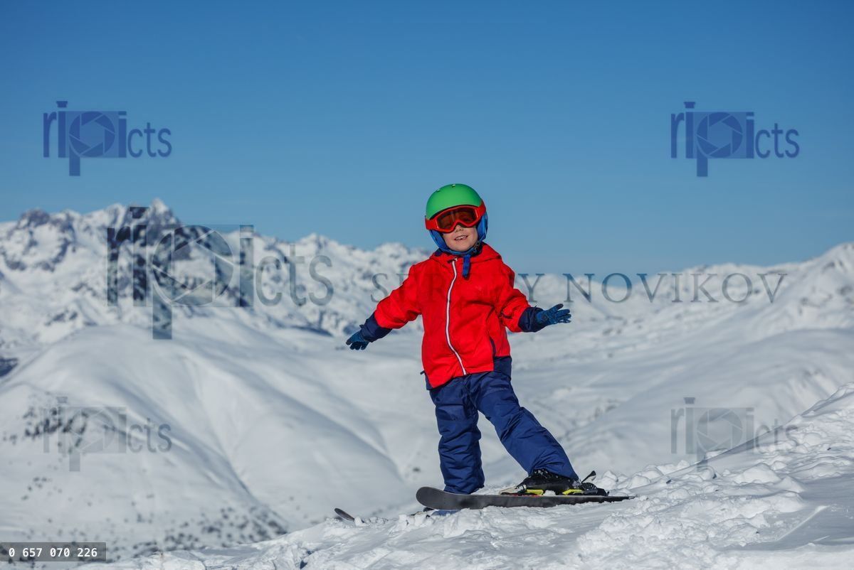 Child in red ski jacket turns while skiing atop a snowy ridge