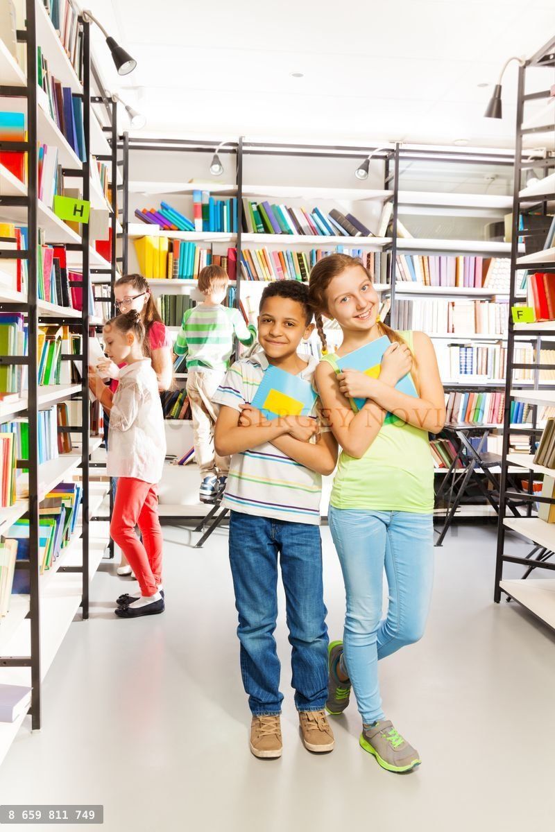 Girl and boy with books stand close in library