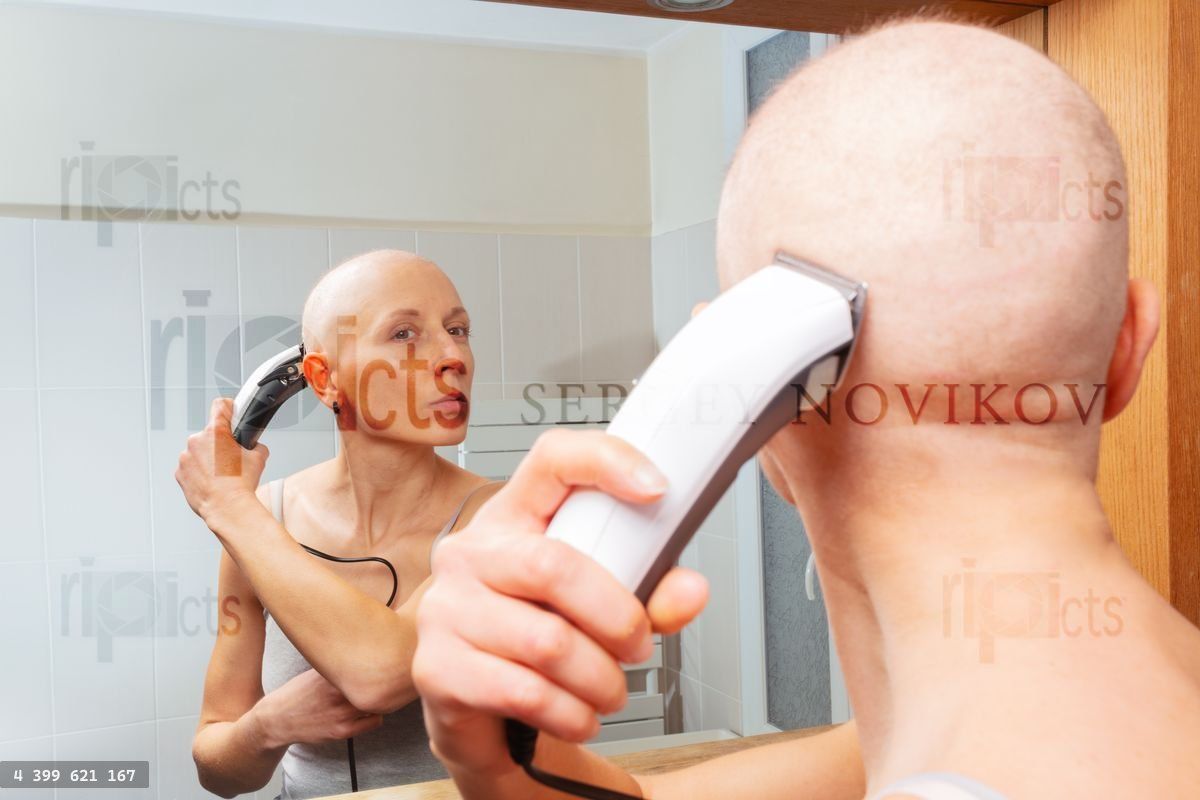 Woman experiencing hair loss uses clippers for head shave
