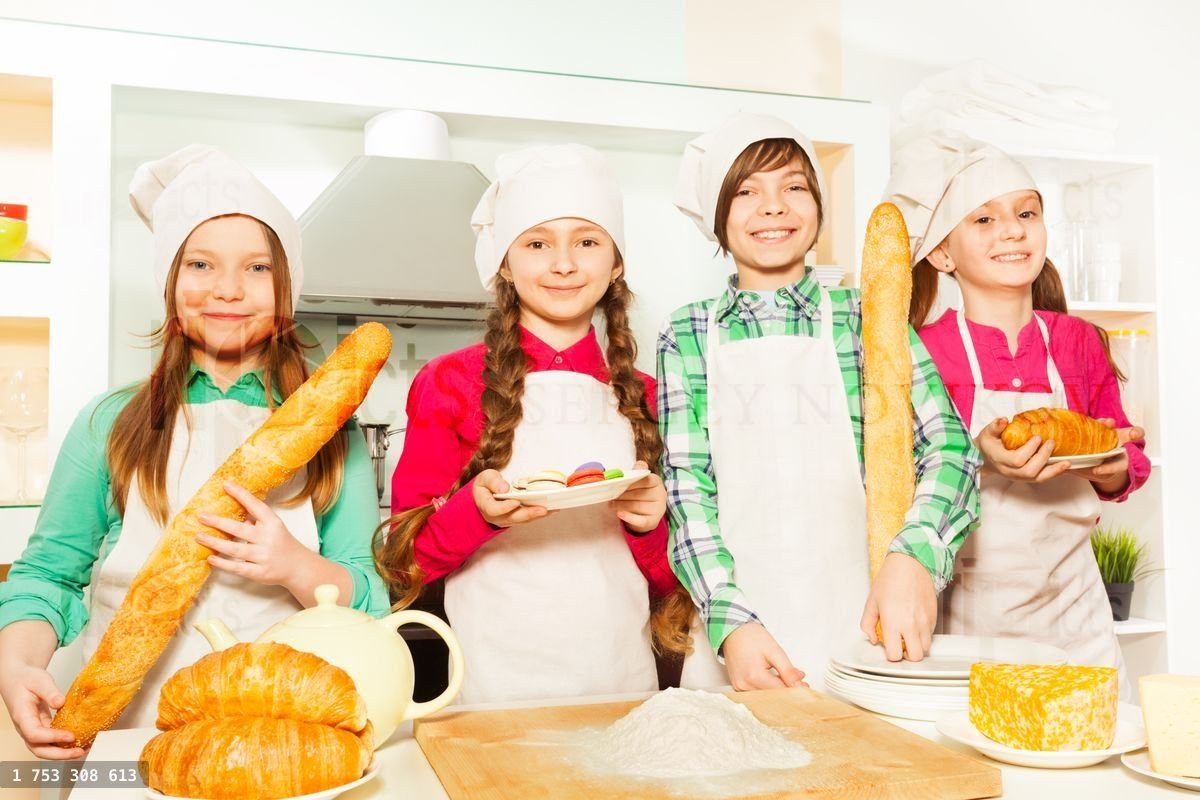 Four young cooks with bakery food at the kitchen