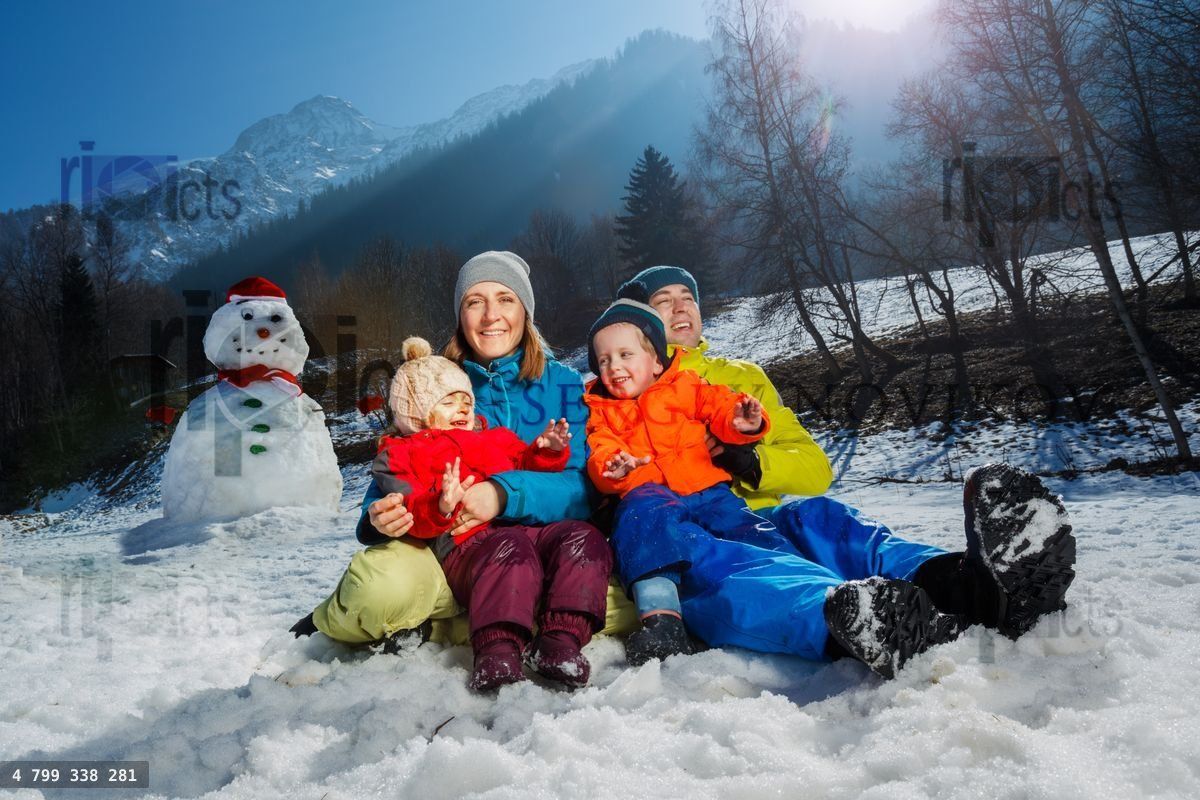 Famille avec deux enfants s'amusant dans la neige, près d'un bonhomme de neige et d'une montagne