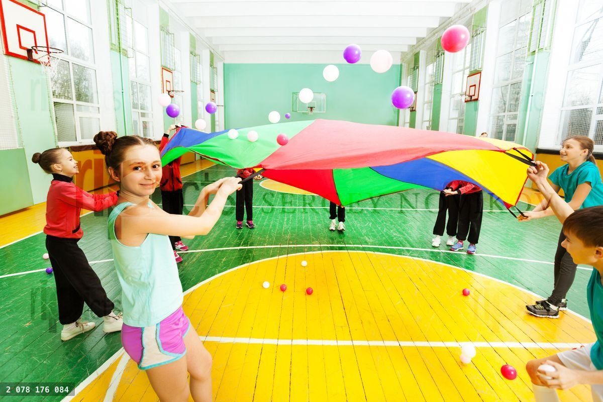 Friends waving parachute with balls in sports hall