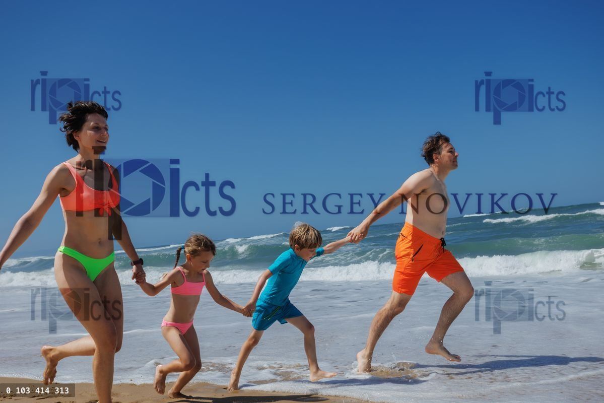 Young parents and kids happily running on the sandy sea shore
