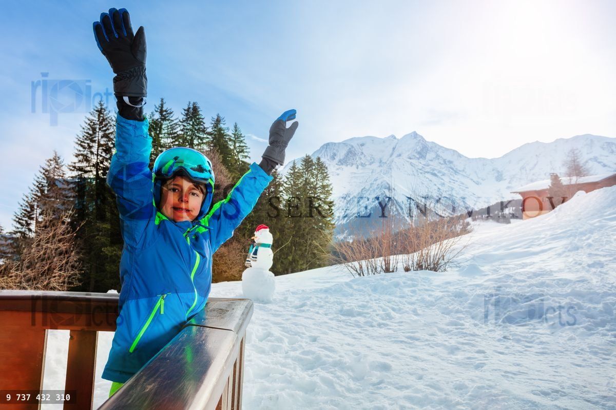 Young boy in ski outfit stand on the balcony lifting hands