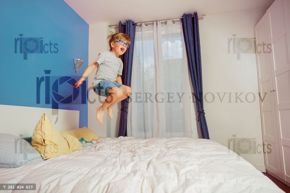 Young boy enthusiastically jumps on bed in a colorful bedroom