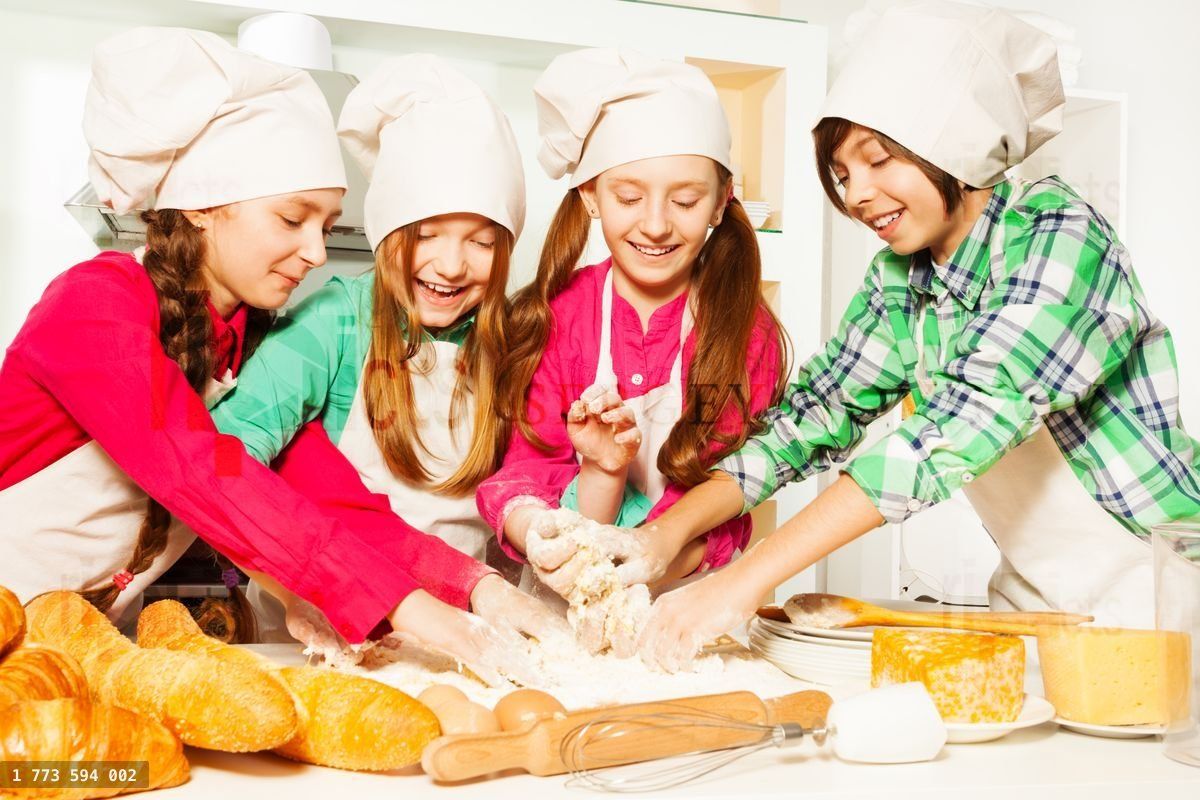 Four young bakers kneading dough at the kitchen