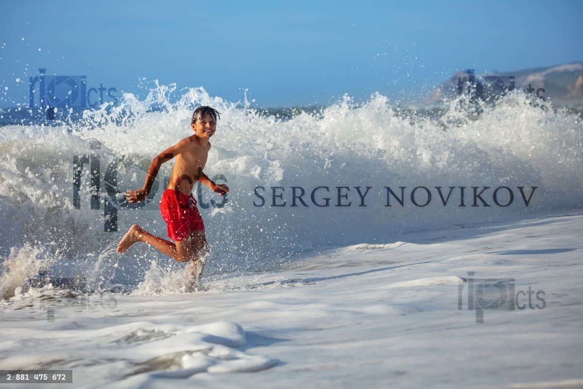 Young boy running along shoreline with ocean waves crash around