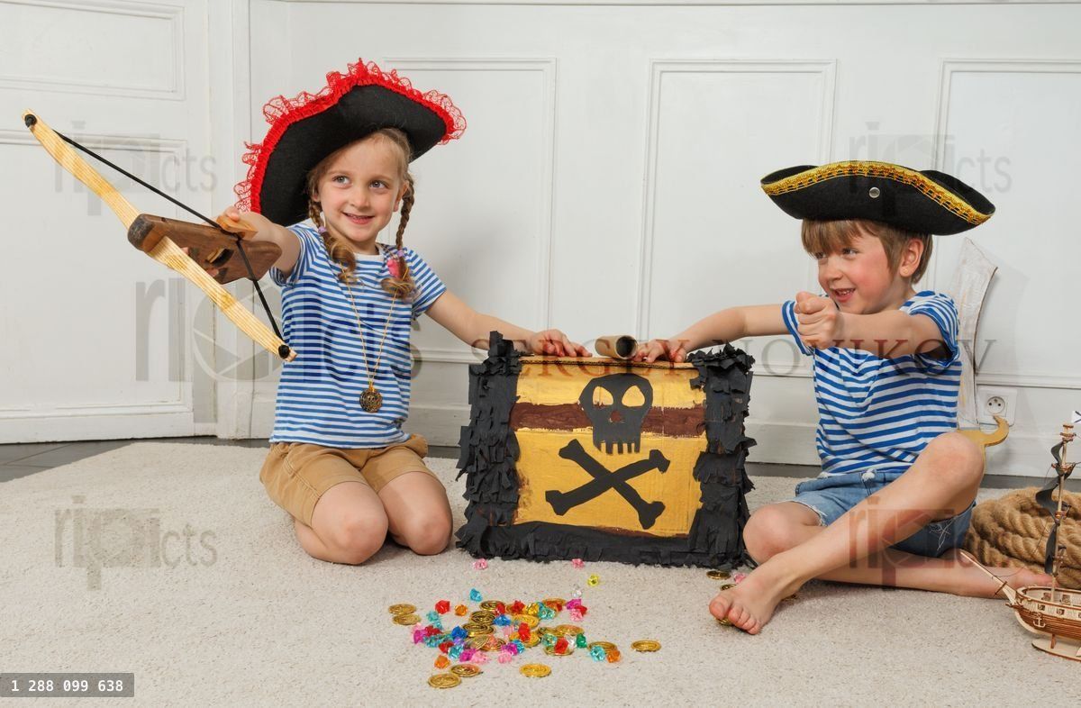 Des enfants pirates visent un arc et une flèche près d'un coffre au trésor marqué d'une tête de mort
