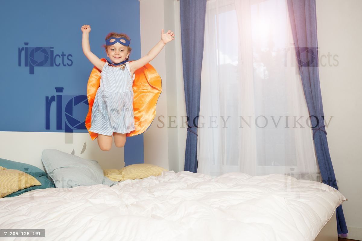Child girl in cape flying through air onto bed, superhero dream
