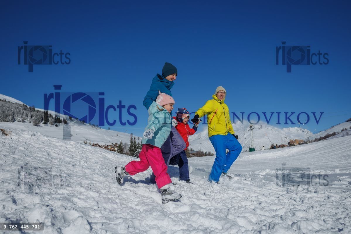 Family strolls together down a snowy hillside under blue sky