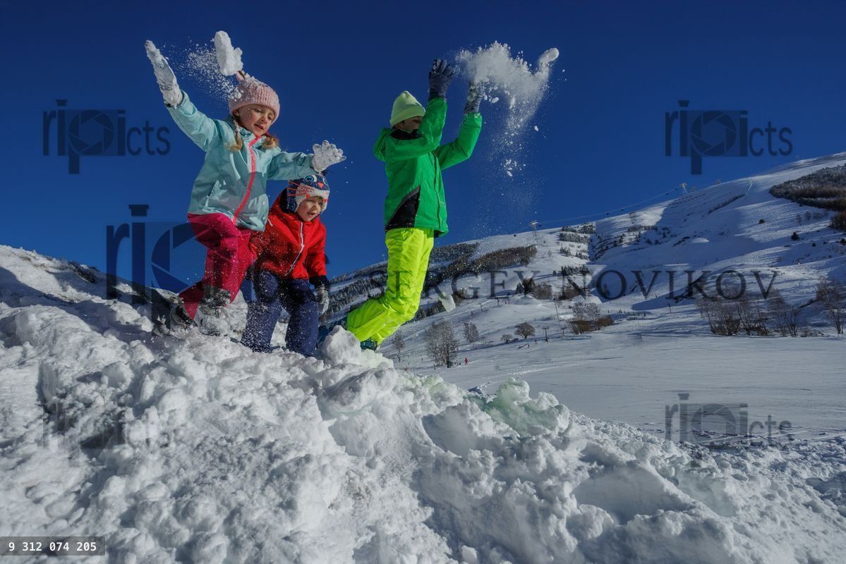 Funny kids toss snow high on a winter slope under bright sky