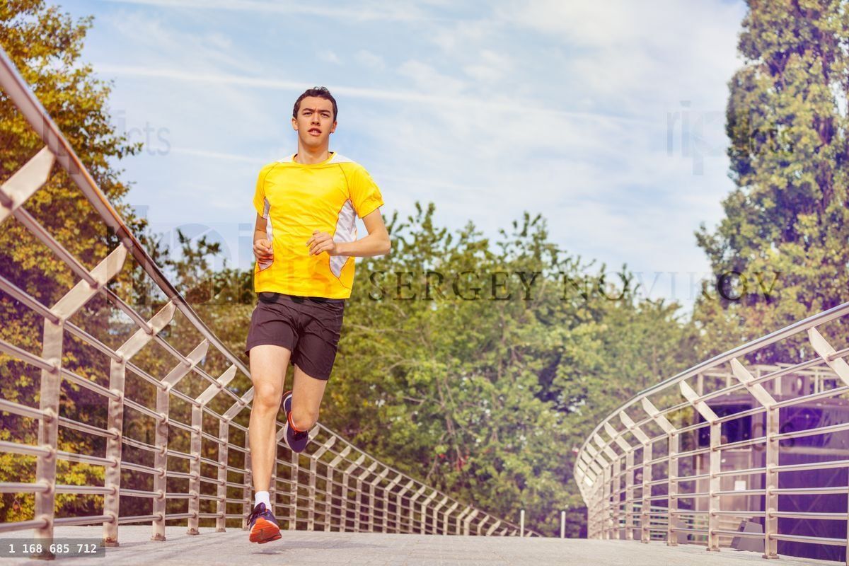 Young man running across the bridge at city park