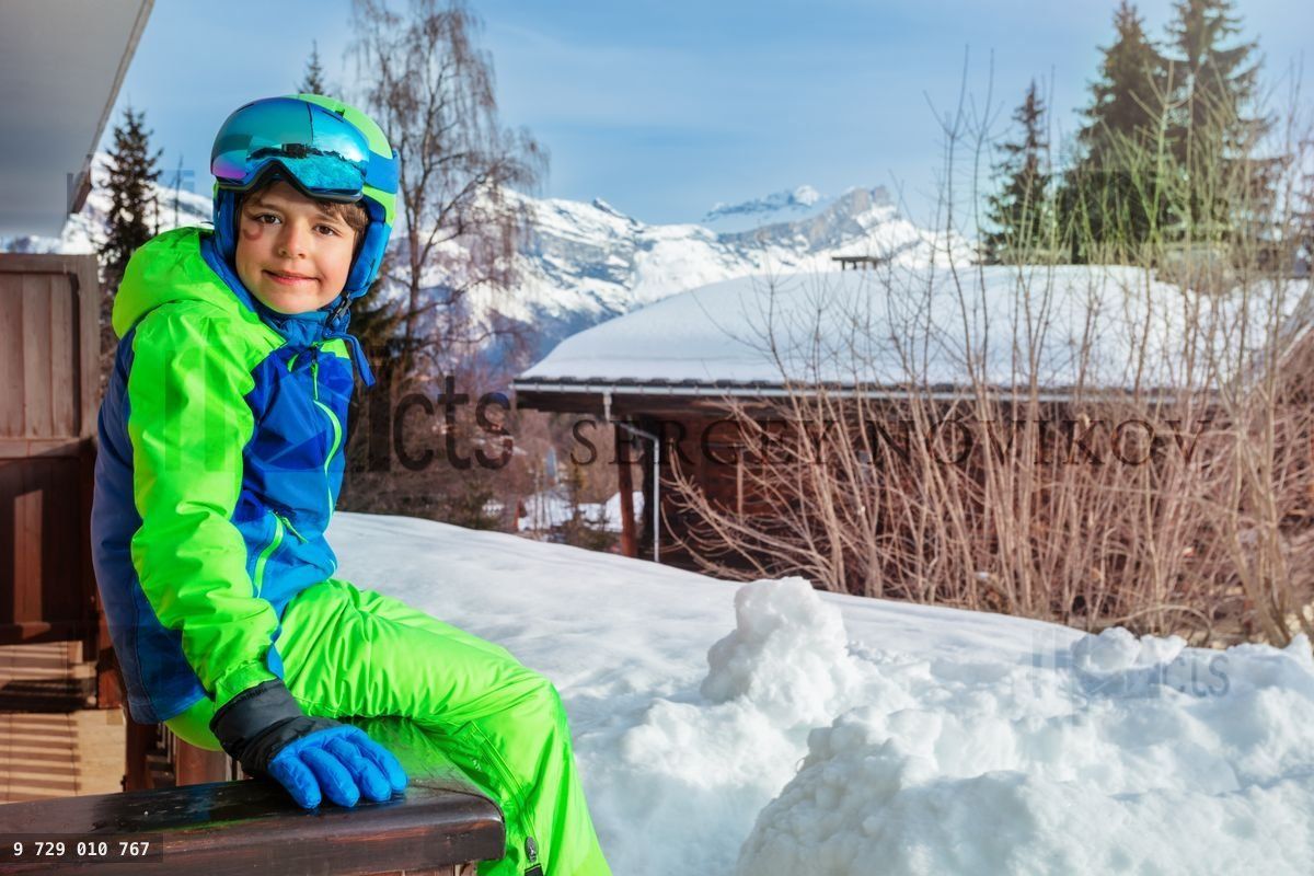 Young boy in ski outfit sit on balcony rail at winter vacations