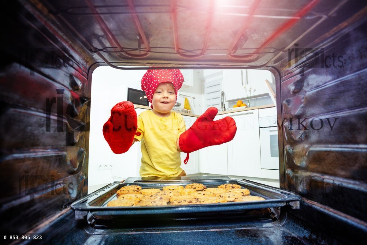 Boy with oven gloves take cookies tray from oven