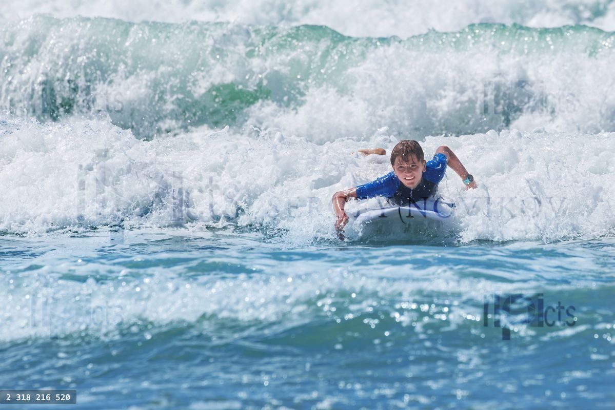 Young boy smile joyfully surfing on a wave at the sunny beach
