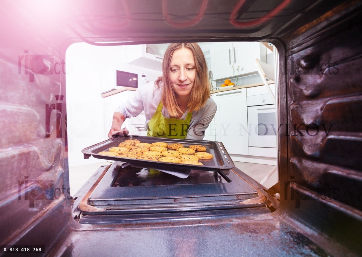 Woman take tray with cookies from oven inside view