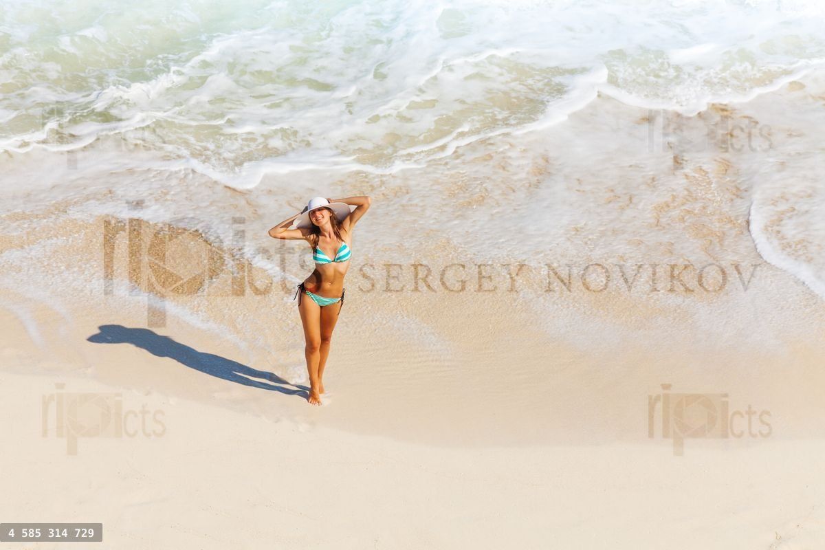 Young woman with white hat stands on ocean sand