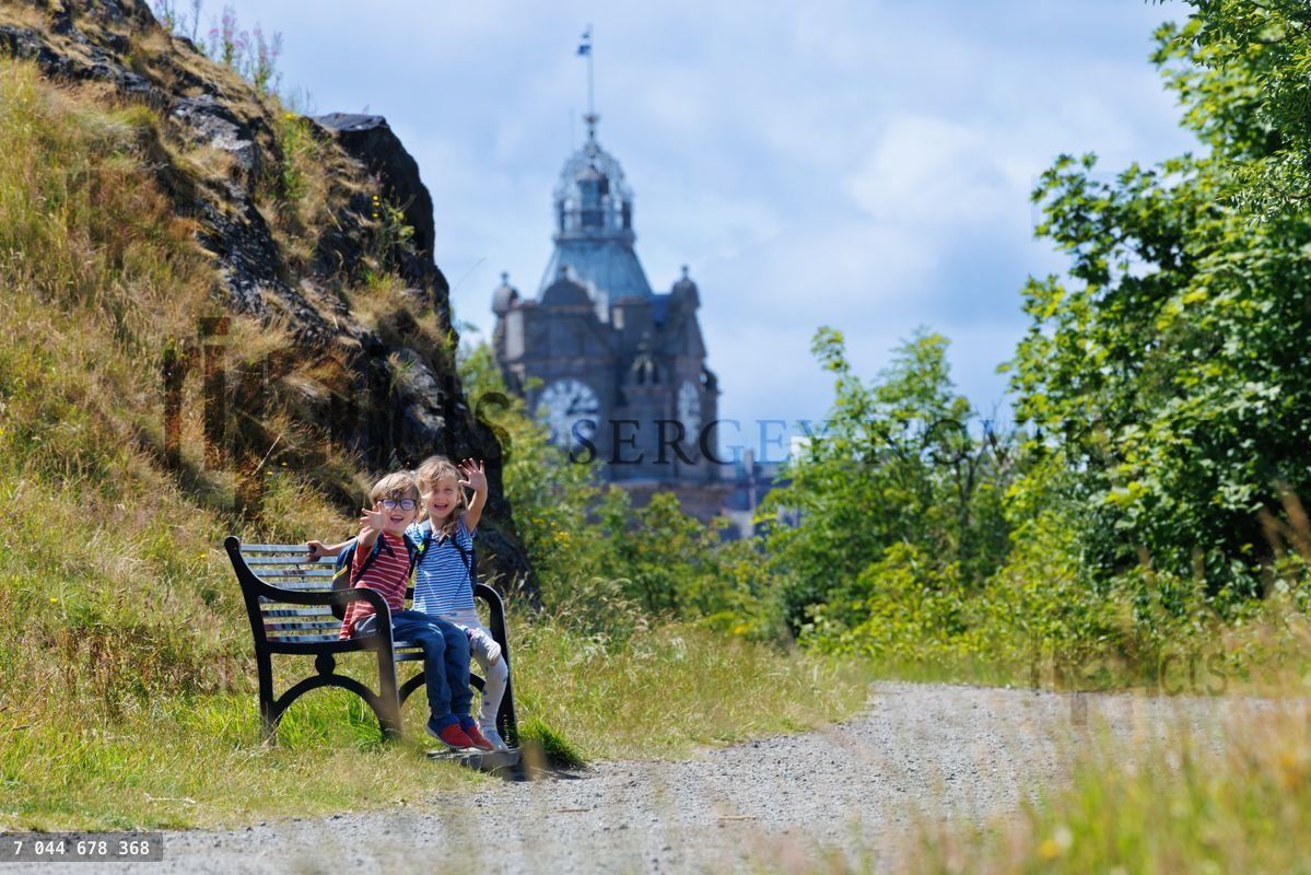 Des enfants font signe depuis un banc de parc avec des vues panoramiques et un beffroi
