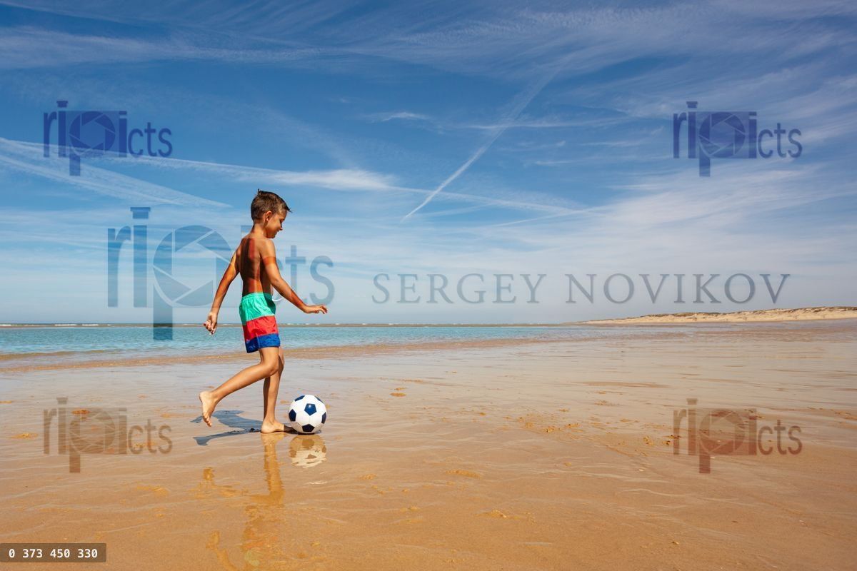 Young boy with soccer ball play on sea beach