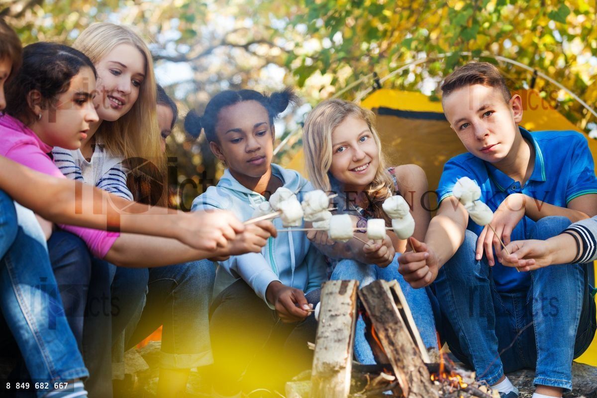 Friends hold marshmallow sticks near bonfire